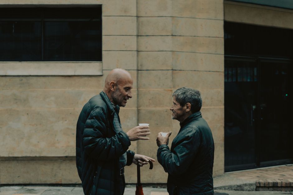 Dos hombres mayores con chaquetas conversando en una calle de Bogotá, compartiendo un momento cálido.