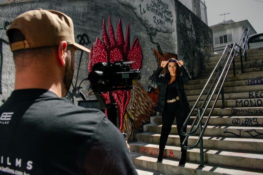 Photographer capturing a woman posing on graffiti-covered stairs in urban setting.
