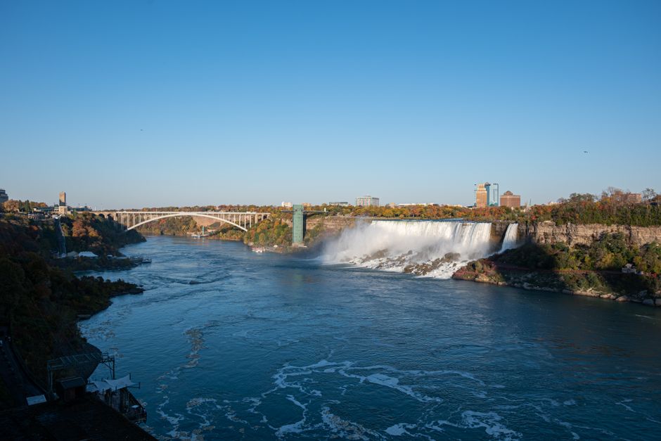 Niagara Falls Canada Tour: Helicopter, Boat Cruise & Journey - A breathtaking view of Niagara Falls with Rainbow Bridge in the background during a clear day.