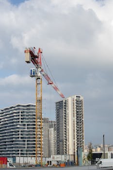 Tower crane operating on a building site with high-rise buildings in the city background.