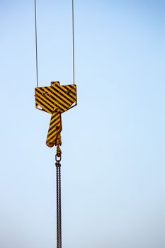 A close-up of a yellow industrial crane hook with striped pattern against a blue sky, symbolizing construction.