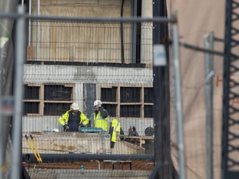 Construction workers in safety gear on an active building site, wearing high-visibility jackets and helmets.