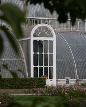 A vintage Victorian glasshouse surrounded by lush greenery and flowers at Kew Gardens, London.