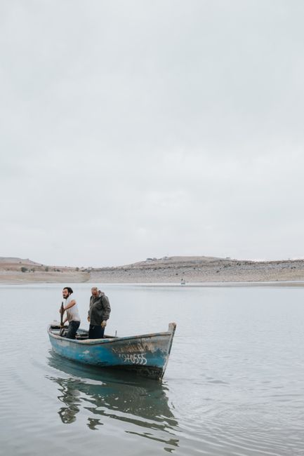 Two men paddling a small boat on a calm lake, set against a peaceful natural landscape.