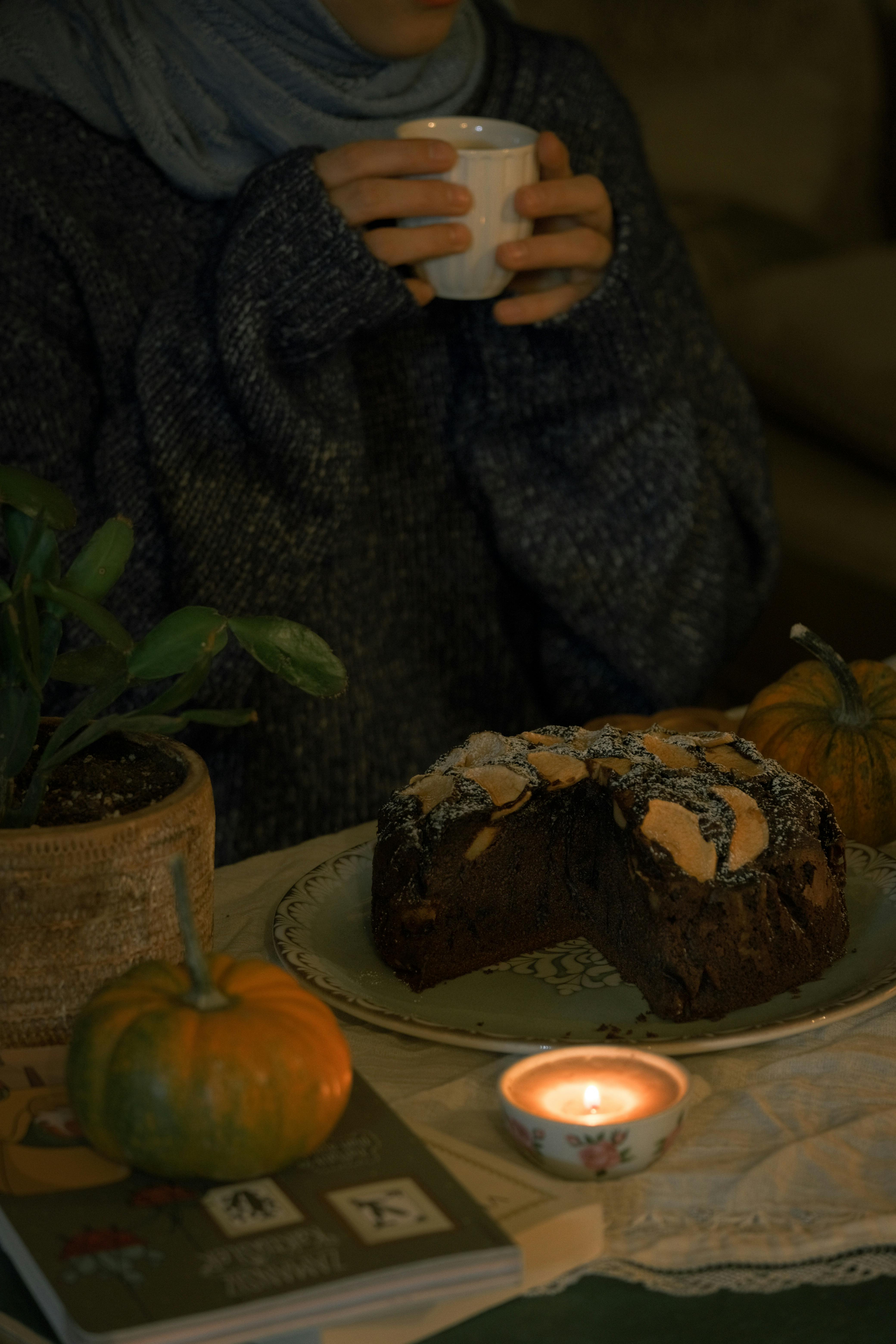 person holding cup in hands near cake and wax candle