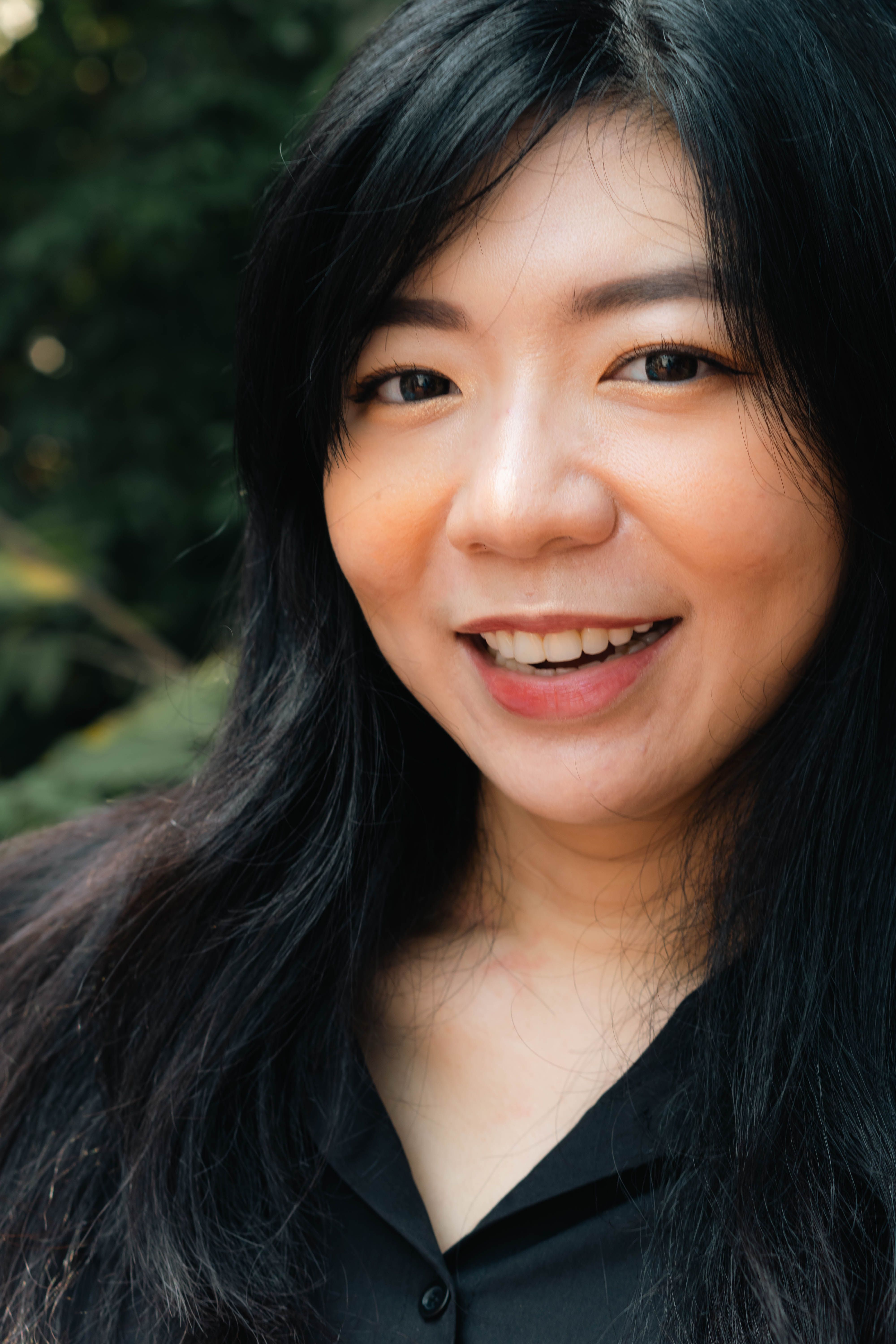 Close-up portrait of a smiling woman with black hair outdoors in natural light.