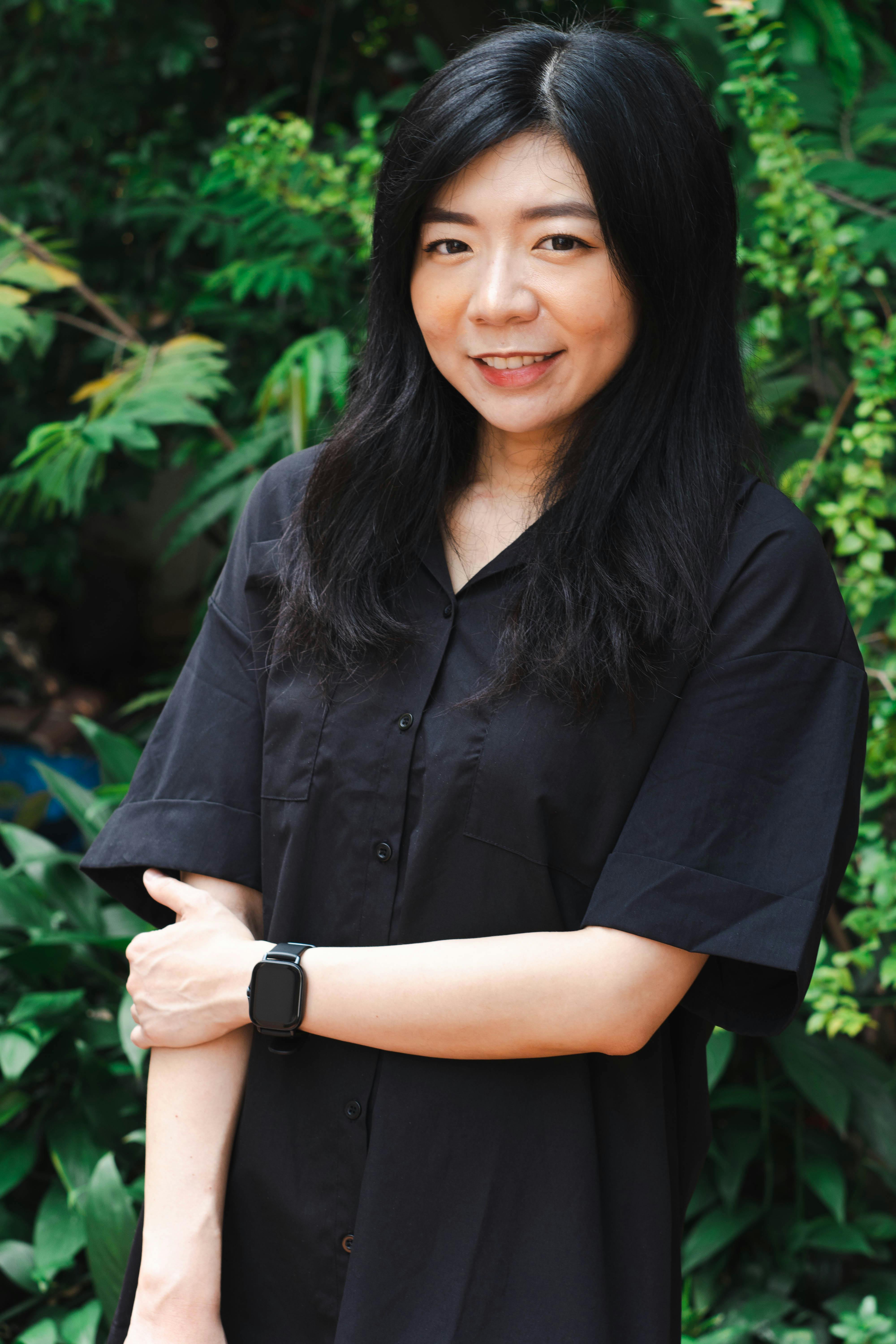 Asian woman smiling confidently in a lush green outdoor setting.