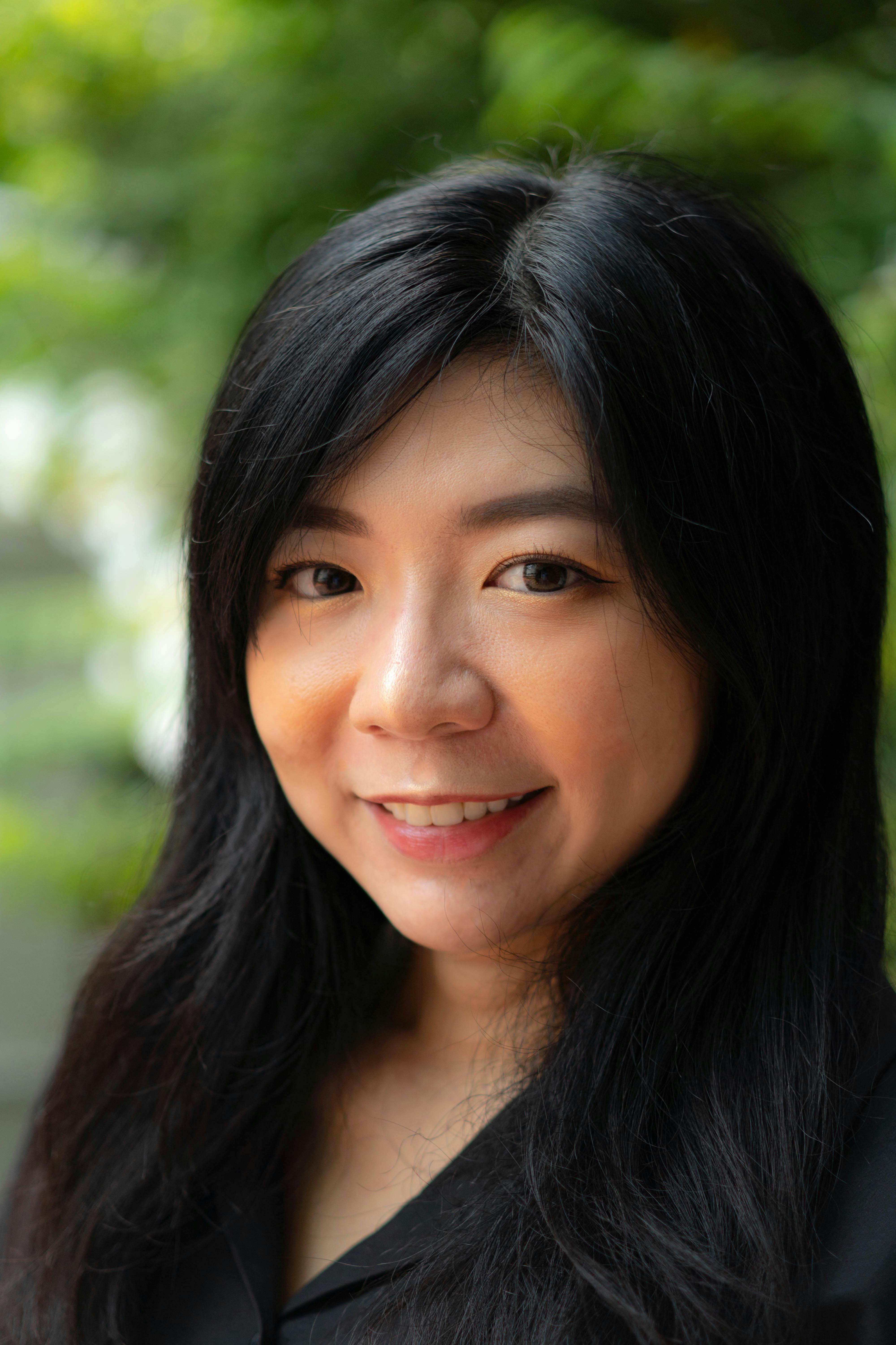 A cheerful woman with long black hair smiling in an outdoor setting.