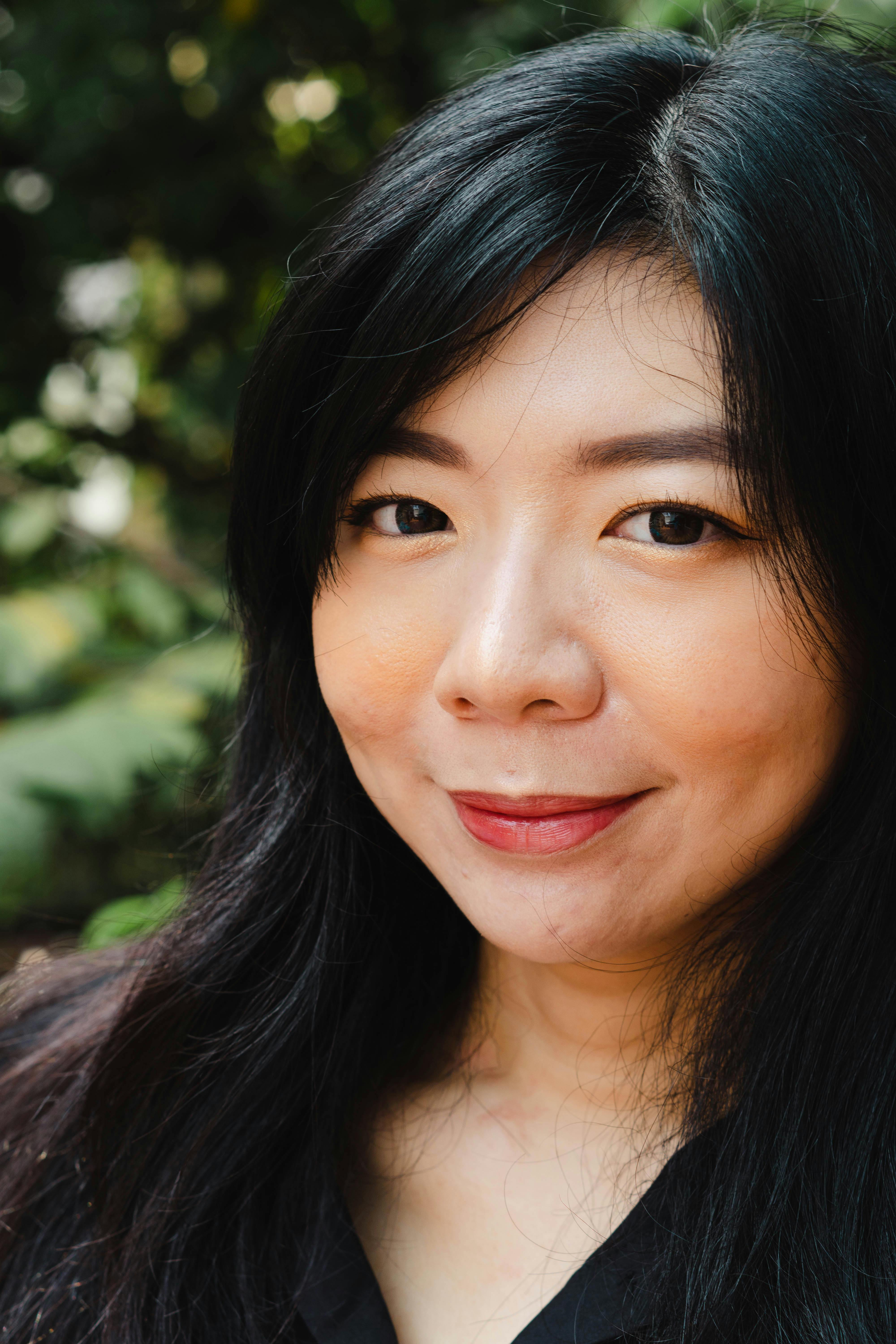 Beautiful close-up of a smiling woman with long hair, surrounded by greenery, embodying a natural and joyful mood.