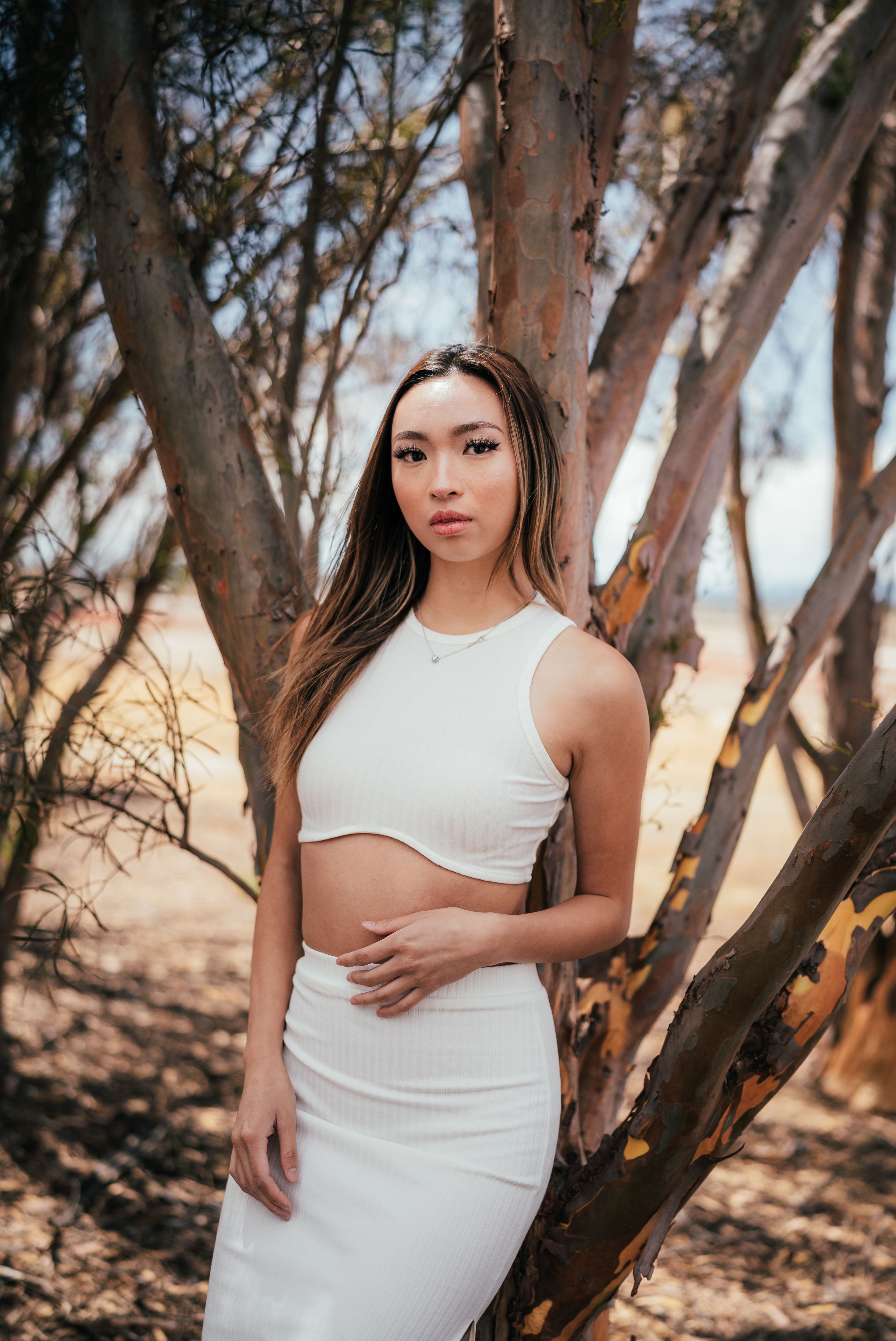 Portrait of a beautiful woman in a white dress standing amongst trees. Bright and serene outdoor setting.