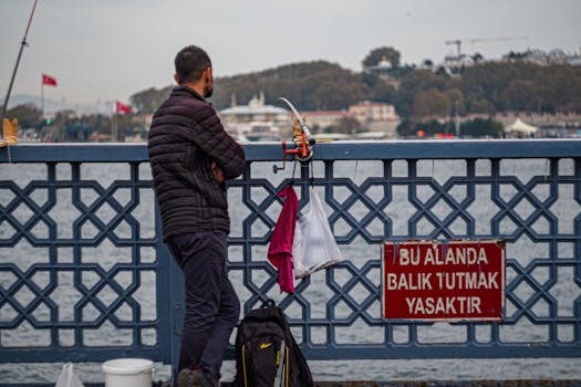 A man stands on a bridge in Istanbul with a fishing rod at a prohibited spot.