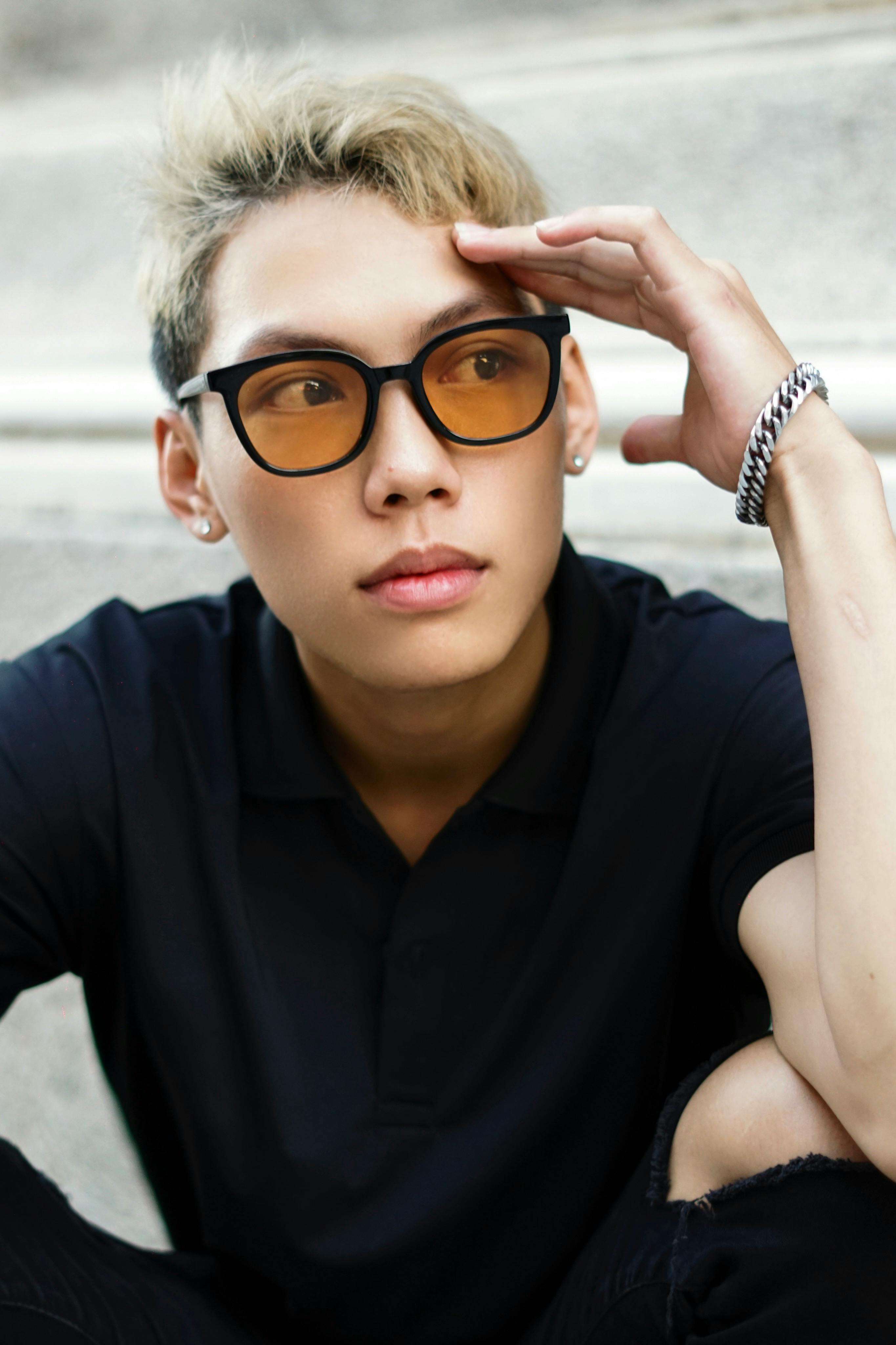 Close-up portrait of a young man wearing glasses, seated outdoors with a thoughtful expression.