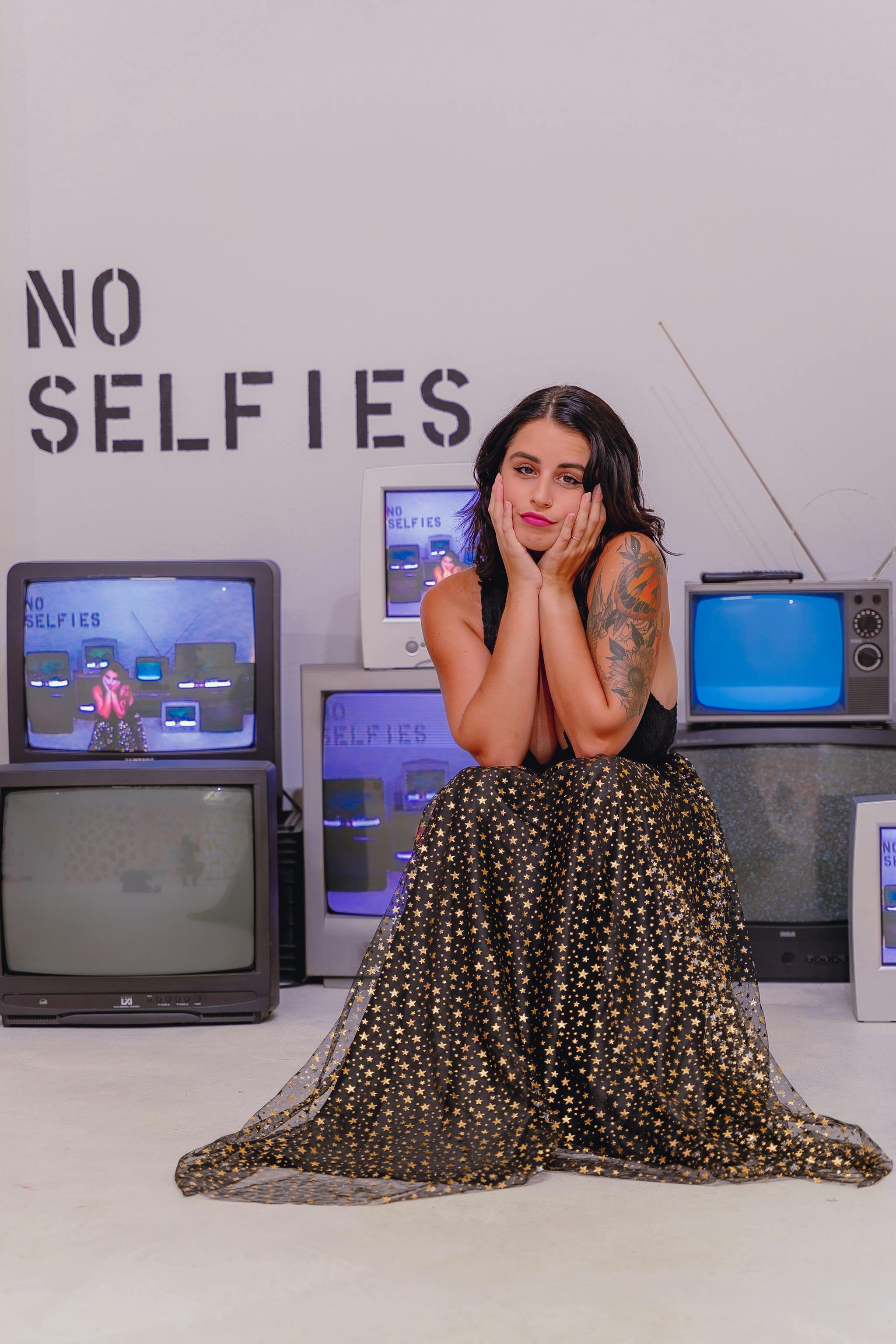 A woman in a retro-styled outfit poses among vintage televisions in a studio setting.