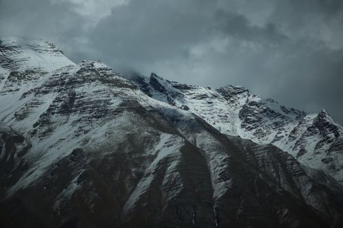 Free Snow-covered mountain peaks captured under a dramatic, cloudy sky, creating a moody winter landscape. Stock Photo