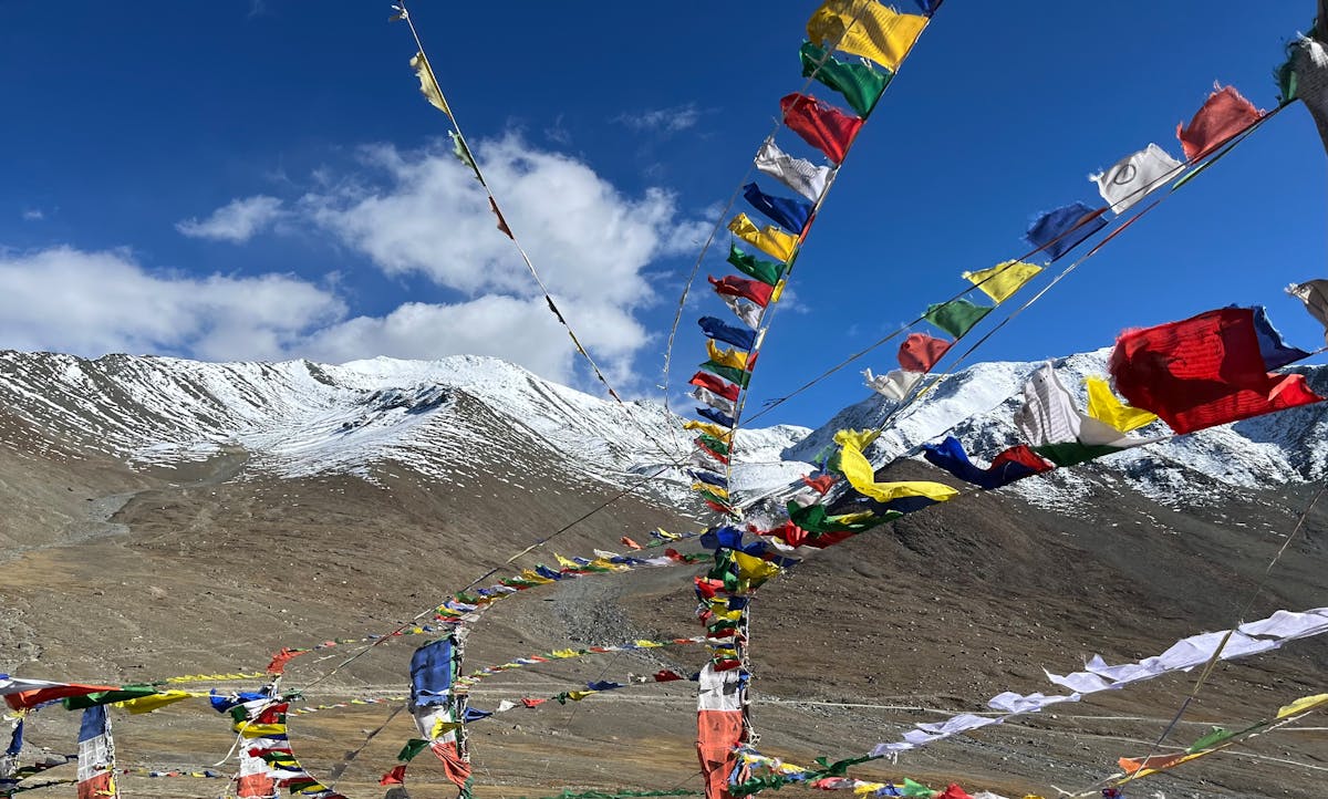 Colourful prayer flags flutter against snowy Himalayan peaks under a clear blue sky