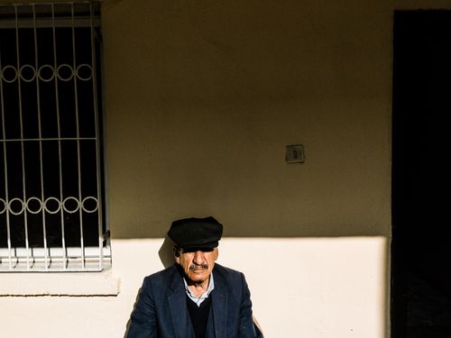 Free Elderly man in black hat sitting against a sunlit wall in Adana, Turkey, showcasing light and shadow contrast. Stock Photo