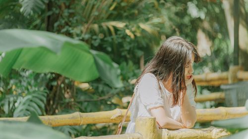 Free Woman in a garden lost in thought, surrounded by lush greenery on a sunny day. Stock Photo