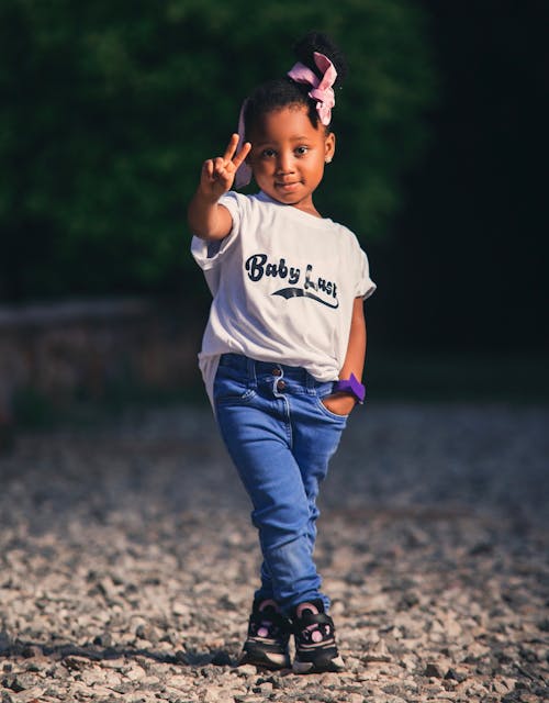 Photo of a Young Girl in a White T-Shirt and Jeans Showing Victory Sign
