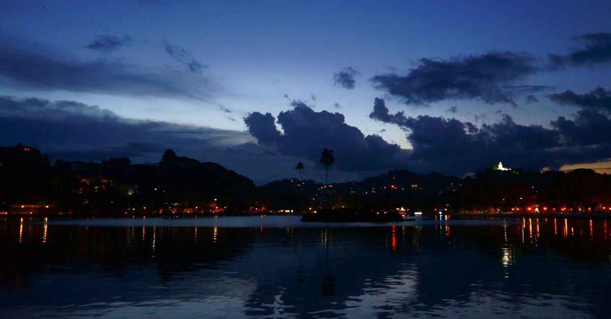 A serene dusk scene over Kandy Lake with vibrant reflections and silhouettes.