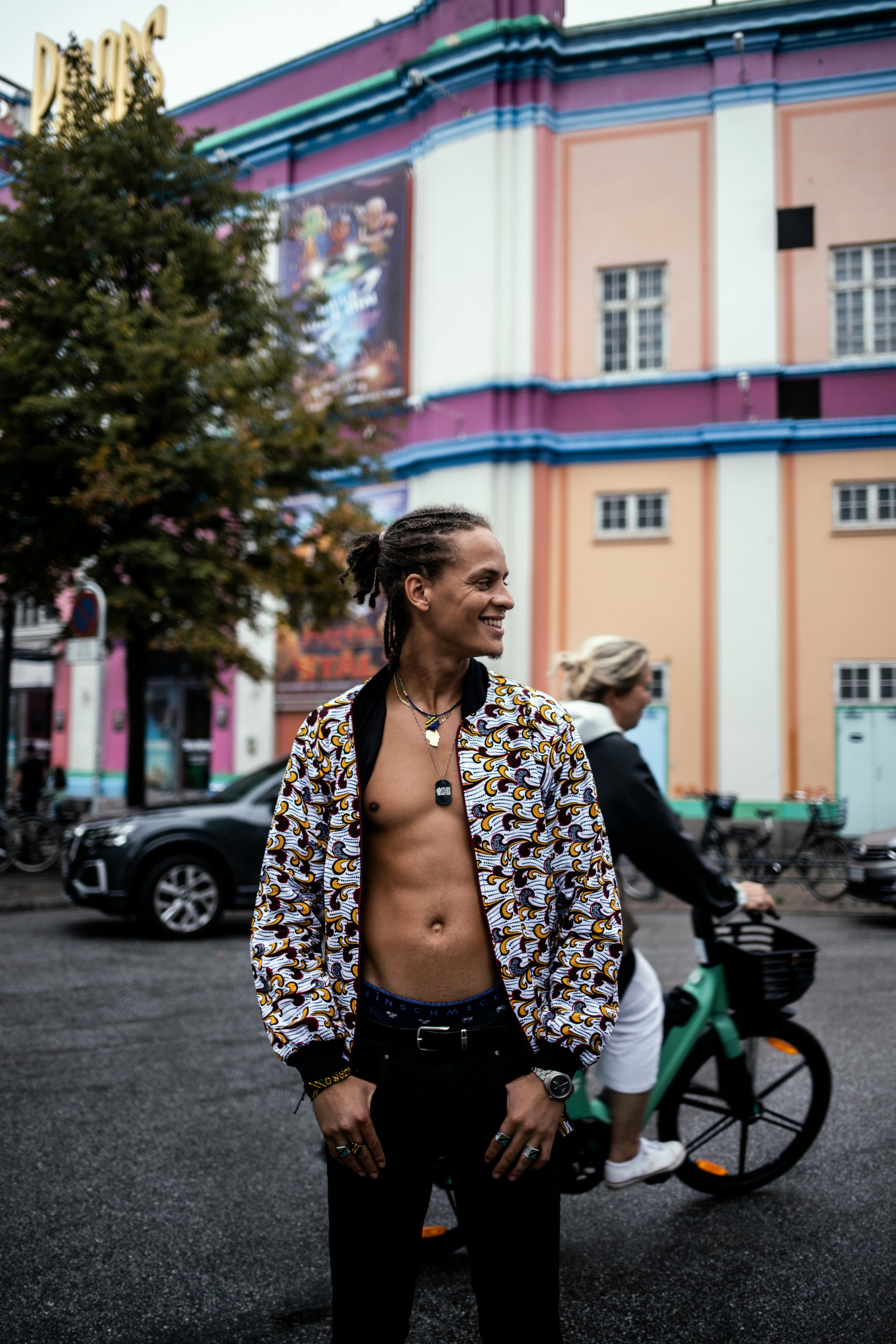 Man in stylish jacket with bicycles and colorful urban backdrop.