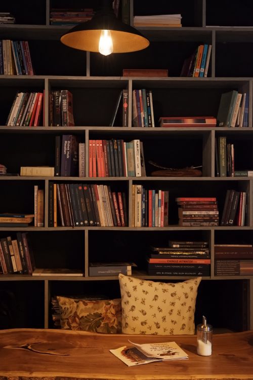 Free A warm illuminated bookshelf with books and a wooden table creates a cozy study atmosphere. Stock Photo