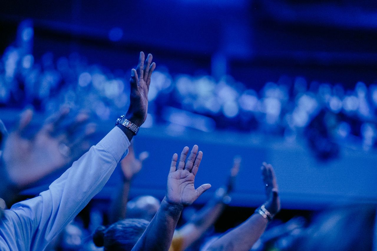 Attendees with hands raised under stage lighting at a keynote session — photo by Luis Quintero on Pexels
