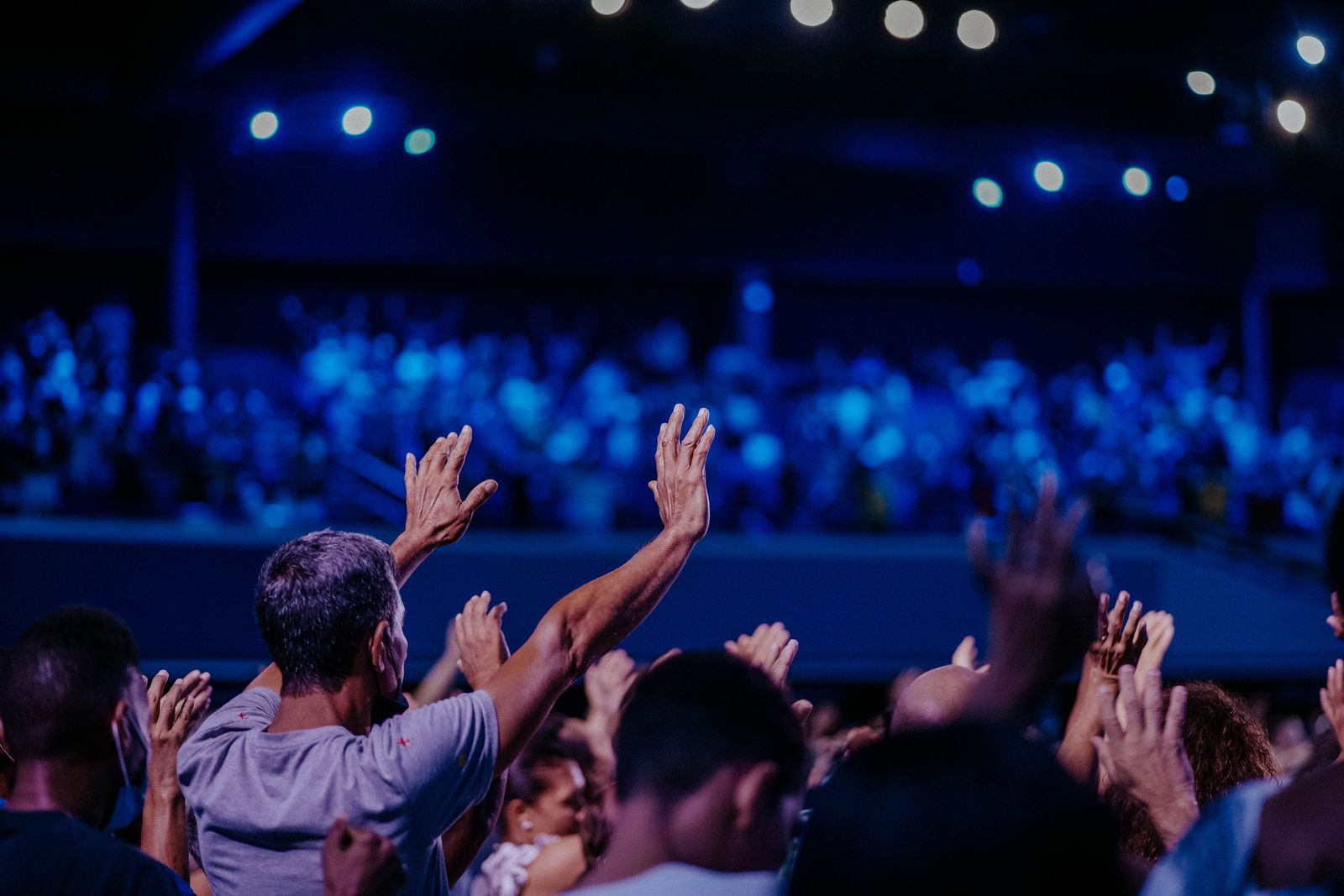 A young crowd worshipping together with hands raised under stage lighting.