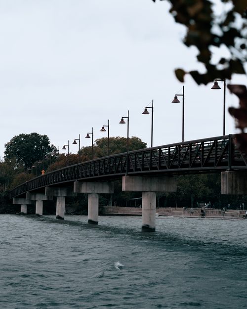 Free A serene view of a bridge with moody sky, street lights, and river. Stock Photo