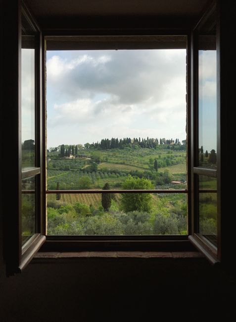 View of San Gimignano's lush hills and vineyards through an open window in Tuscany.