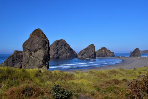 Free Scenic view of a rocky beach with grass, waves, and rock formations under a clear blue sky. Stock Photo