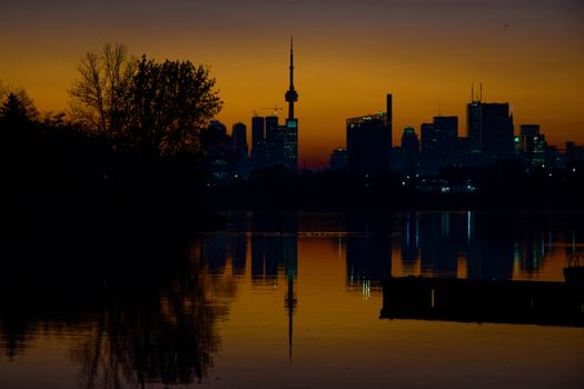 Stunning sunset view of Toronto skyline with reflections on water and vibrant sky.