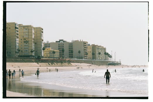 Cádiz beachfront with cityscape and beachgoers enjoying a sunny summer day.