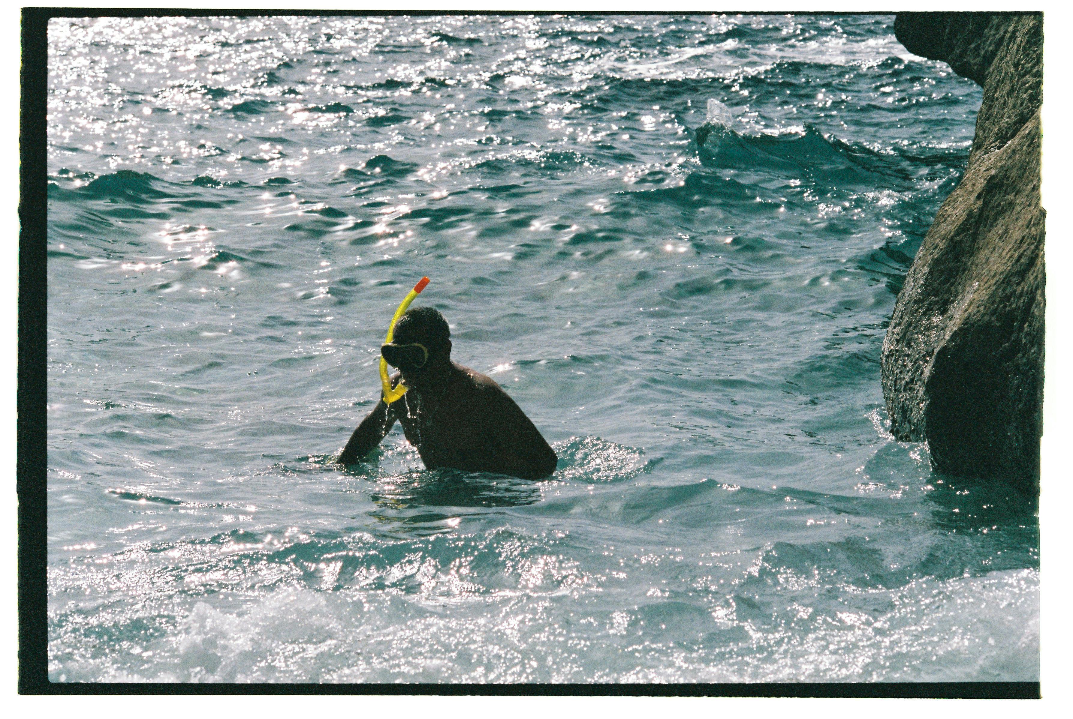 A snorkeler ventures into the sparkling blue sea of Ibiza, Spain, near coastal rocks.