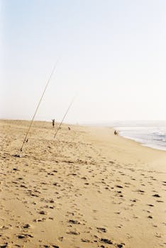 Tranquil beach with fishing rods and footprints in Tocha, Portugal, under a clear sky.