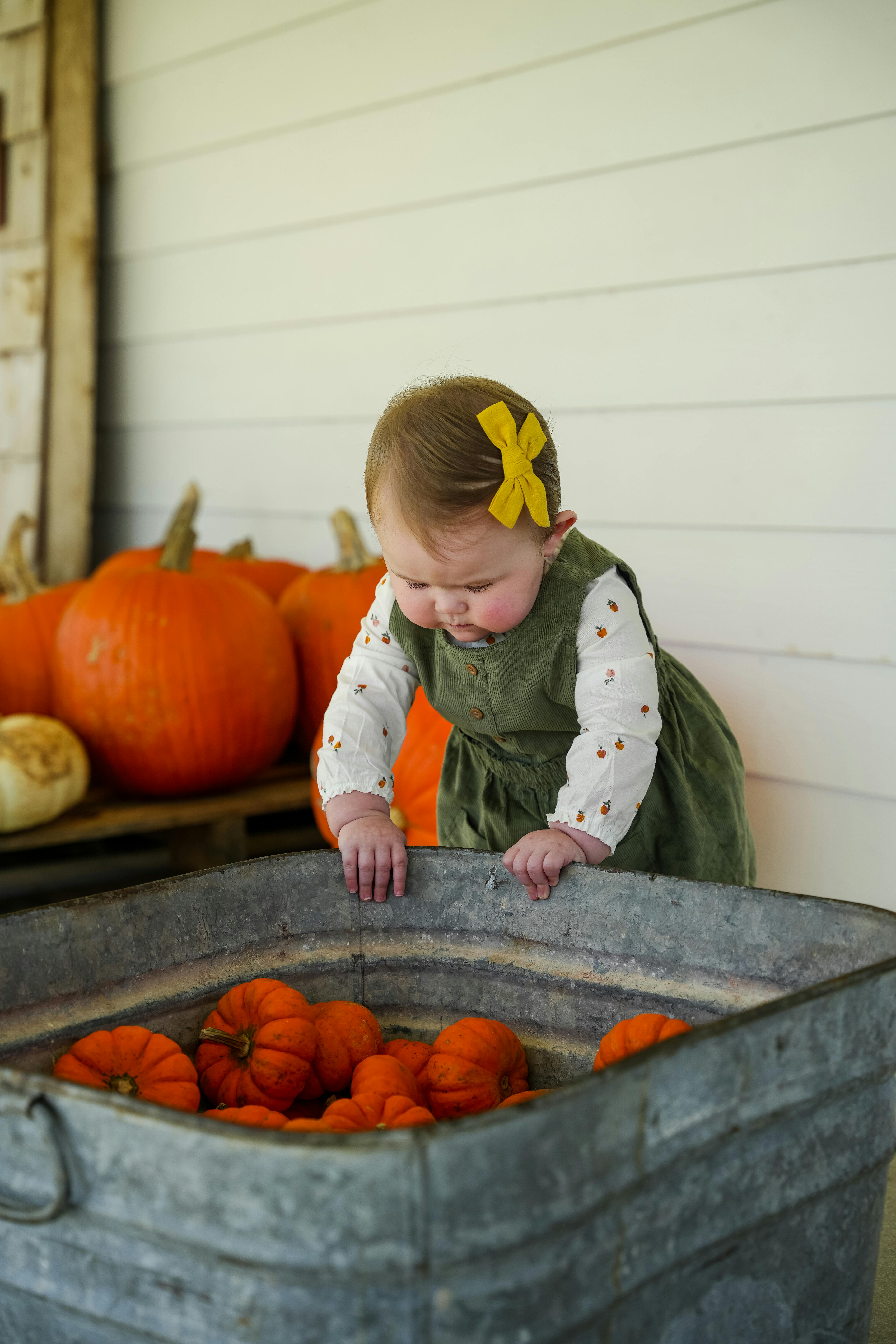 A young girl in a green dress explores pumpkins on a rustic porch.