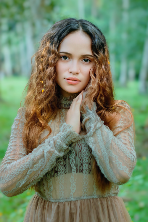 Free A young woman with curly hair poses in a lace dress outdoors, exuding elegance and grace. Stock Photo