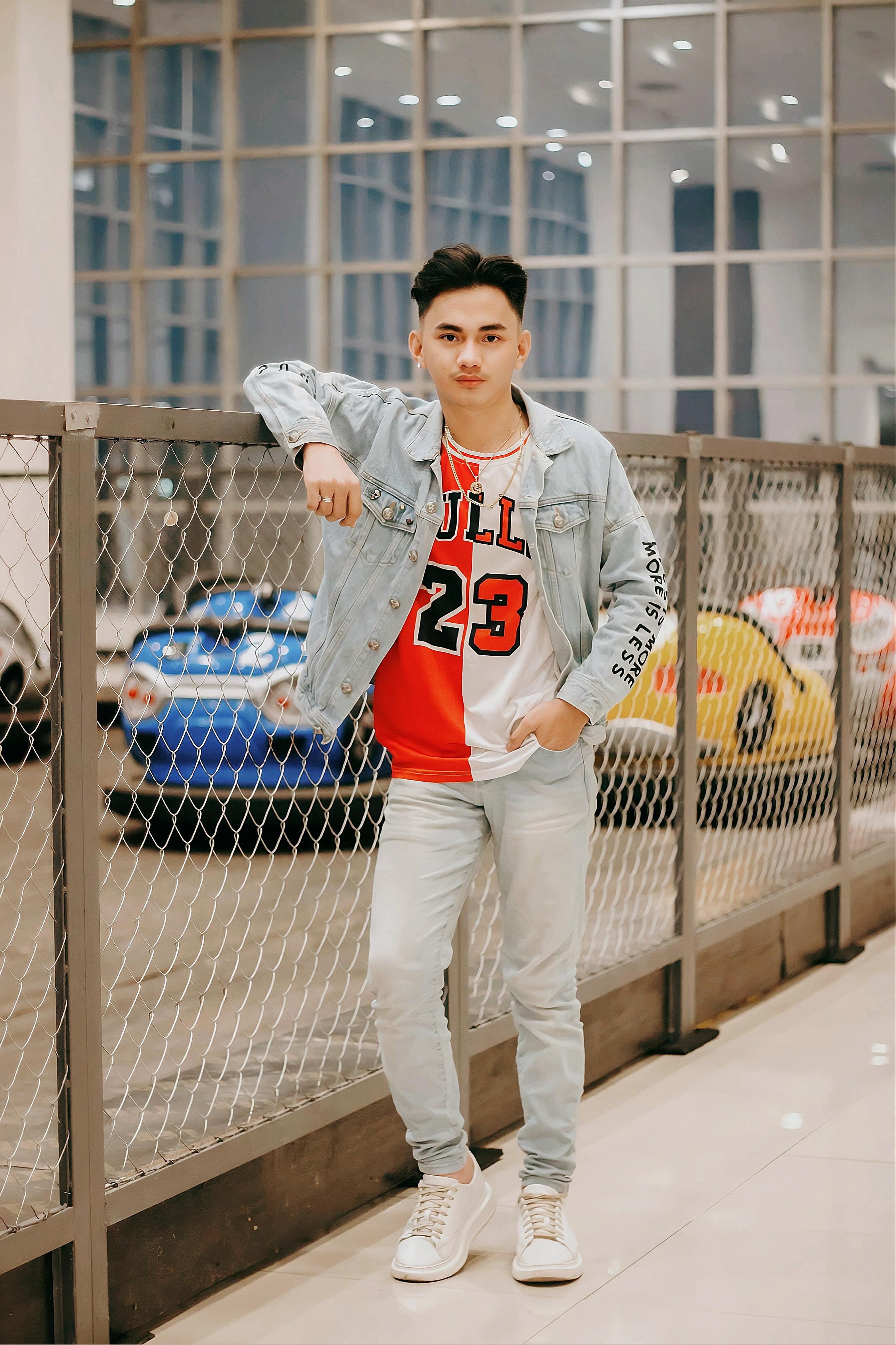 Teenage male in stylish fashion by a chain-link fence, exuding confidence.
