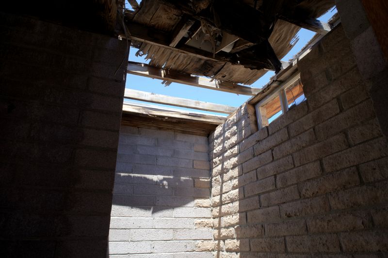 Interior of an abandoned building with a broken roof allowing daylight in, highlighting decay and shadows.