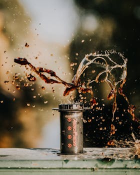 Vibrant capture of coffee splashing from an AeroPress in a natural setting, perfect for lifestyle and beverage themes.