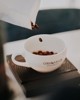 Close-up shot of coffee beans falling into a white cup, highlighting coffee culture and freshness.