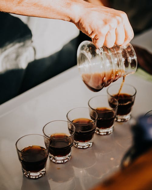 Free A Person Pouring Black Coffee on Clear Glasses Stock Photo