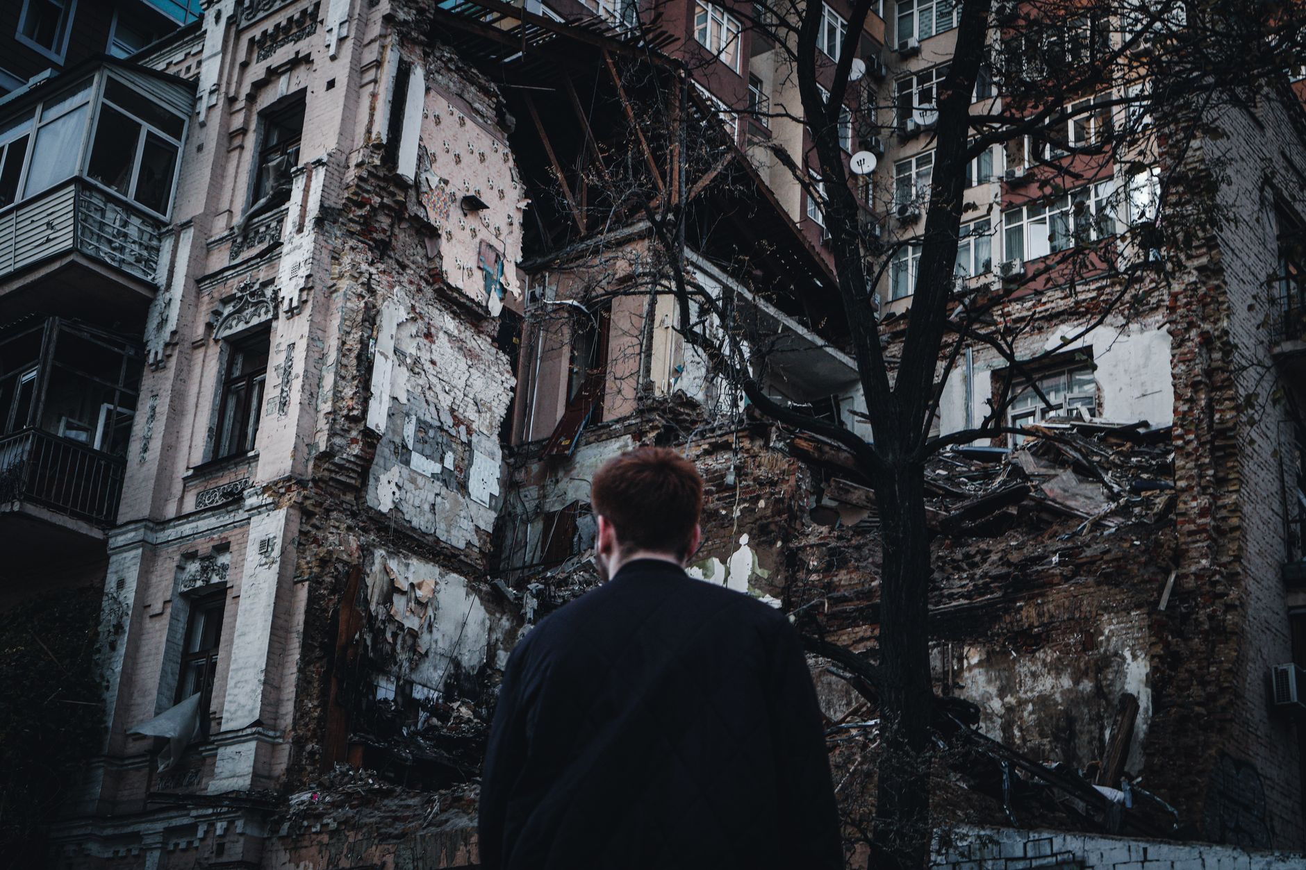 A man looks at a damaged residential building in Kyiv, Ukraine, highlighting urban destruction and resilience.