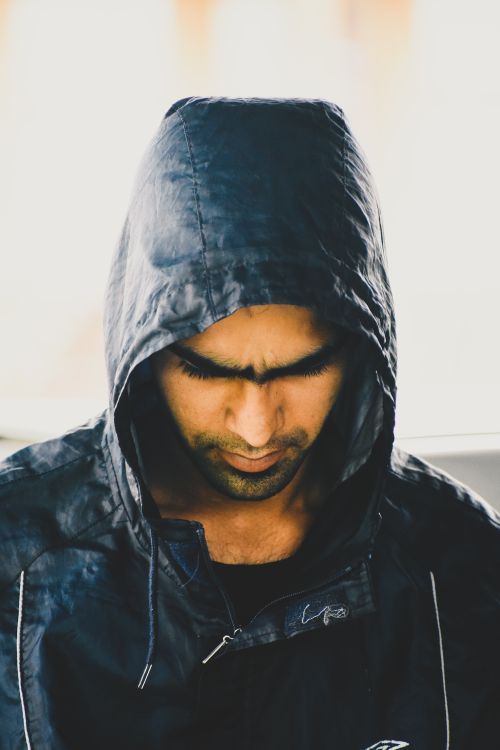 Free Portrait of a man wearing a hooded jacket, looking down introspectively indoors. Stock Photo