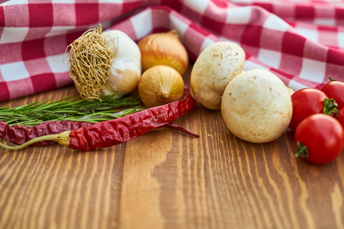 Fresh onions, garlic bulbs and tomatoes on a checked cloth, showing high-fructan foods that cause bloating