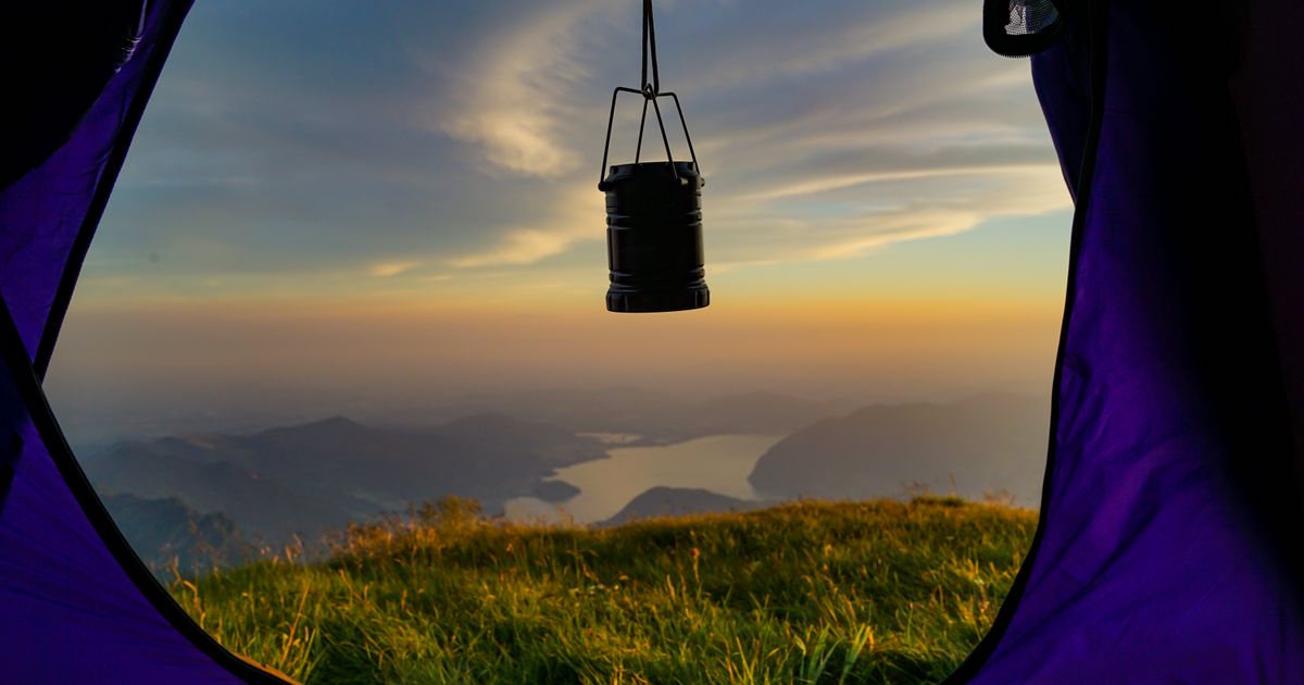 A camping lantern hanging in a tent doorway at sunset