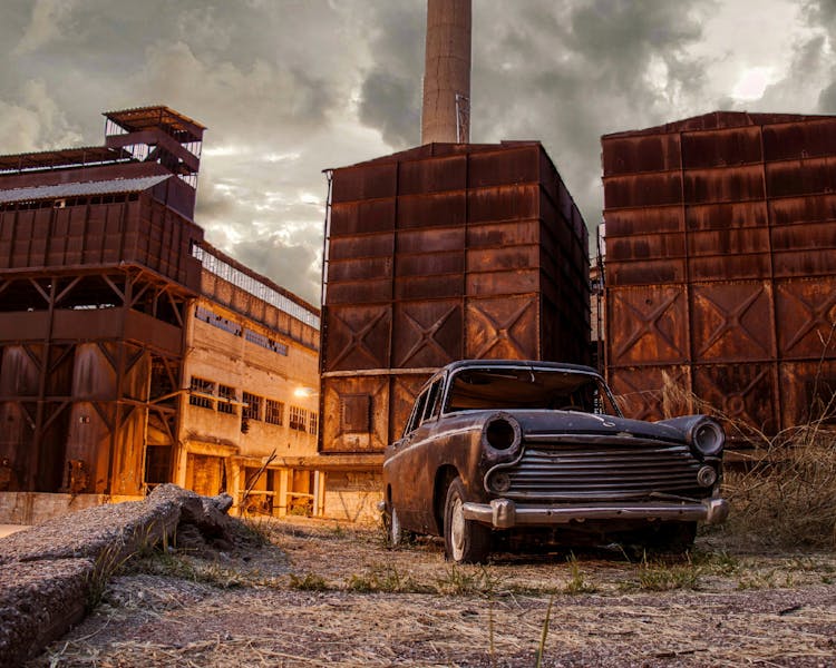 An Abandoned Car Parked Near The Factory Buildings