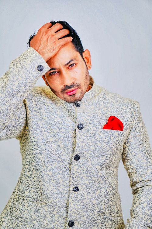 Free Portrait of an adult man posing confidently in a patterned suit with a red pocket square, hand on hair. Stock Photo