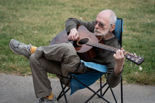 Elderly Man Playing Guitar While Sitting on Camping Chair