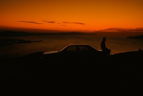 Man Sitting on Car at Sunset