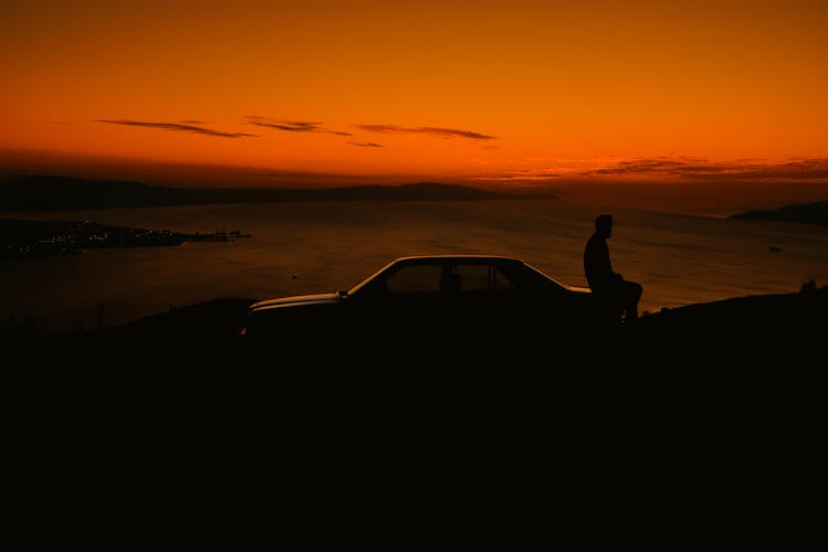 Man Sitting On Car At Sunset